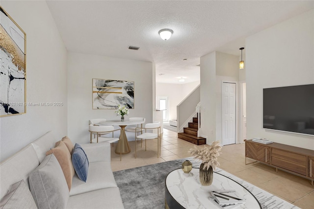 living room featuring a textured ceiling, stairway, light tile patterned flooring, and visible vents