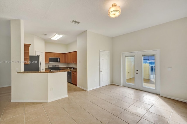 kitchen with brown cabinets, stainless steel appliances, dark countertops, visible vents, and a peninsula