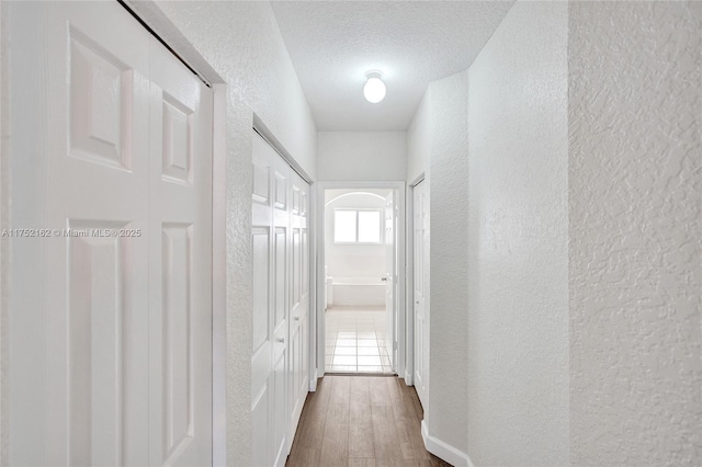 corridor with a textured ceiling, a textured wall, and dark wood-type flooring