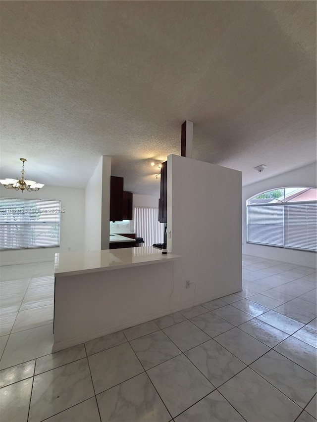 interior space with a textured ceiling, light tile patterned floors, a chandelier, a peninsula, and light countertops