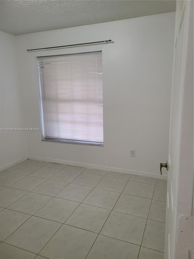 spare room with a textured ceiling, light tile patterned floors, and baseboards