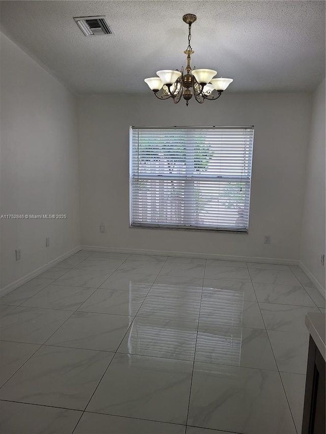 spare room featuring marble finish floor, visible vents, a textured ceiling, and an inviting chandelier