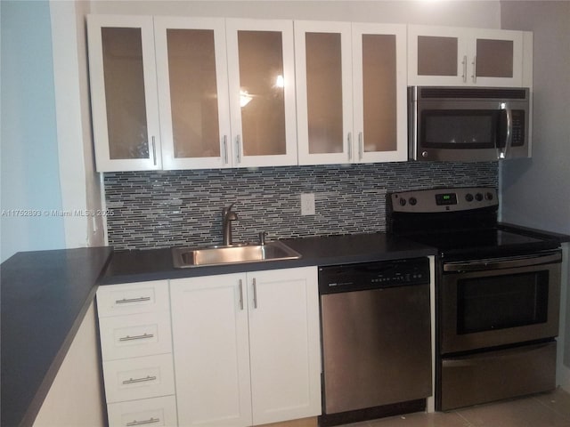 kitchen with appliances with stainless steel finishes, white cabinets, a sink, and backsplash