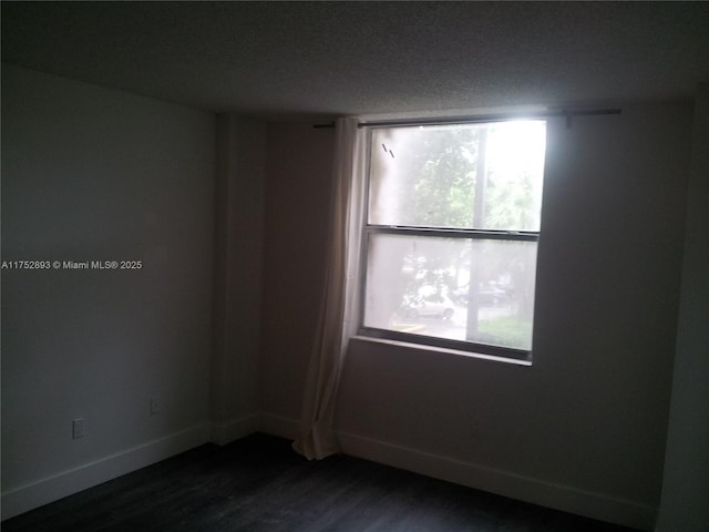 spare room featuring dark wood-type flooring and baseboards