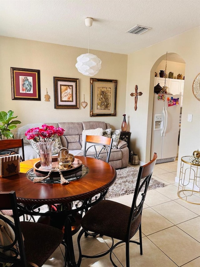 dining area with arched walkways, visible vents, a textured ceiling, and light tile patterned floors