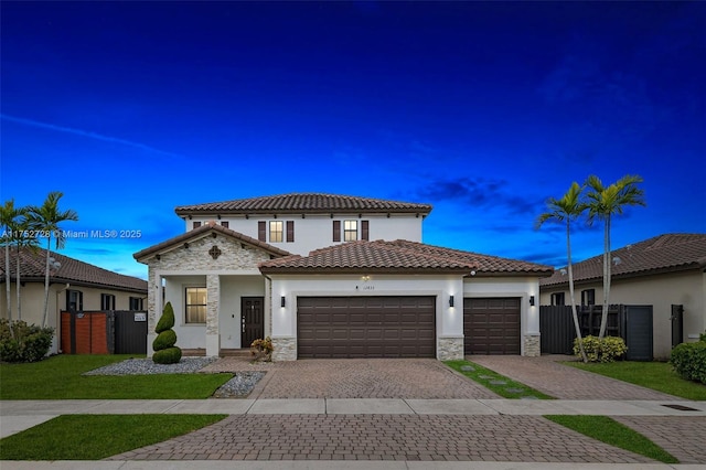 mediterranean / spanish-style home featuring an attached garage, stone siding, fence, and decorative driveway