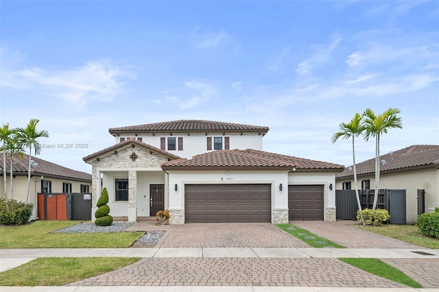 mediterranean / spanish-style home with stucco siding, decorative driveway, stone siding, fence, and an attached garage