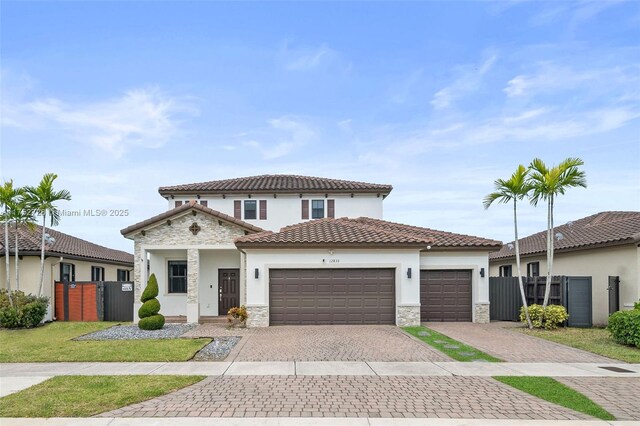 mediterranean / spanish home with fence, an attached garage, stucco siding, stone siding, and decorative driveway