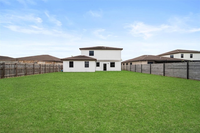 rear view of property with a lawn, a tiled roof, a fenced backyard, and stucco siding