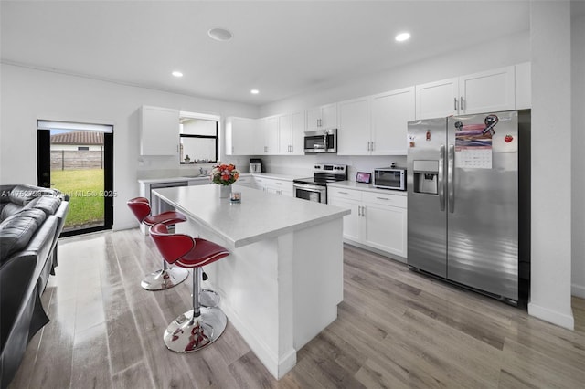 kitchen featuring stainless steel appliances, light wood-style floors, white cabinets, a center island, and a kitchen bar