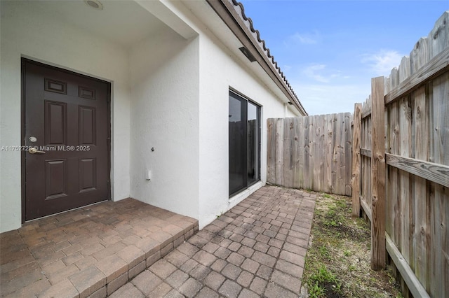 view of exterior entry with a patio area, fence, and stucco siding