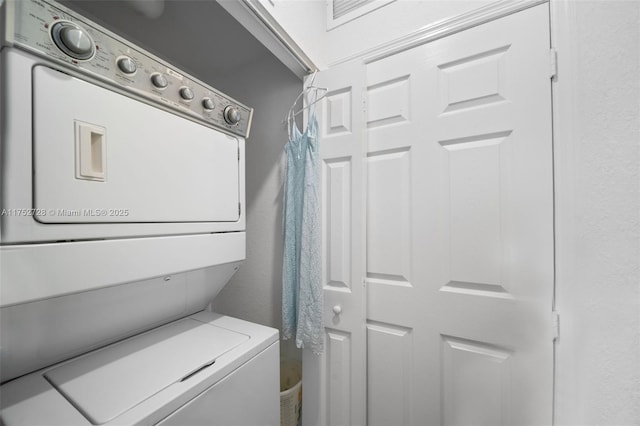 laundry area with laundry area, stacked washer / dryer, and a textured wall