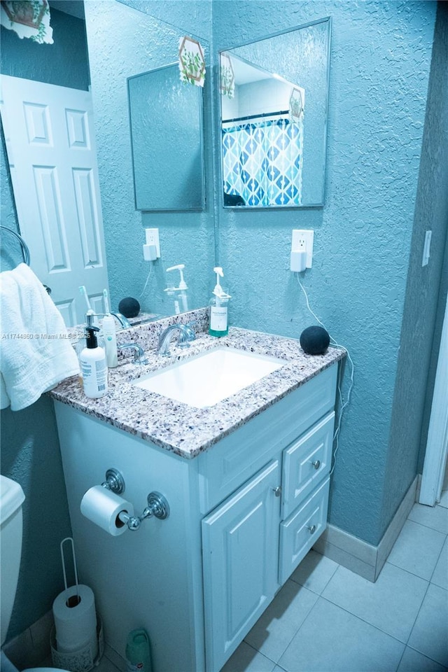 full bath featuring tile patterned flooring, a textured wall, vanity, and toilet