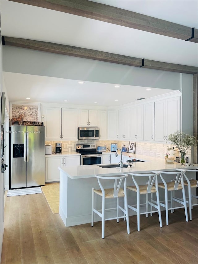 kitchen with stainless steel appliances, white cabinetry, beam ceiling, light wood finished floors, and tasteful backsplash