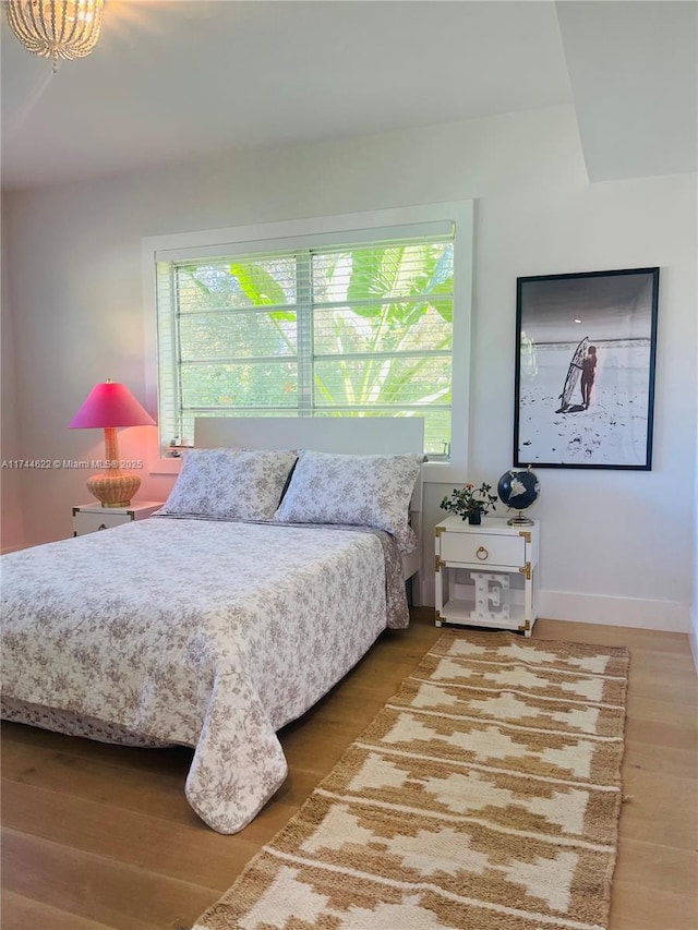 bedroom with multiple windows, wood finished floors, and baseboards