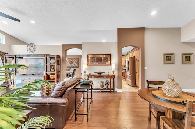 living area featuring a ceiling fan, arched walkways, a textured ceiling, and wood finished floors