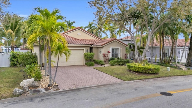 mediterranean / spanish house featuring decorative driveway, a tile roof, stucco siding, an attached garage, and a front yard