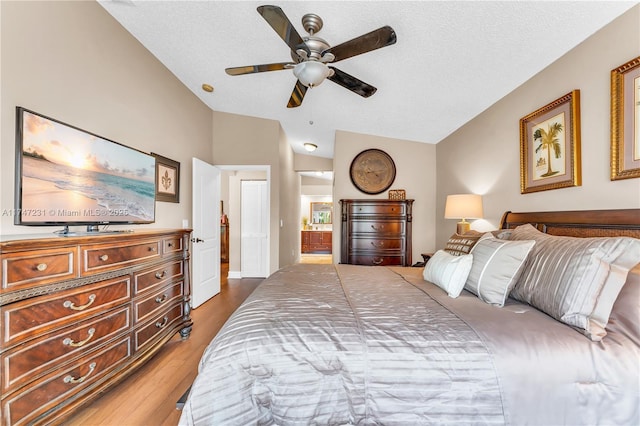 bedroom with lofted ceiling, ensuite bath, ceiling fan, wood finished floors, and a textured ceiling