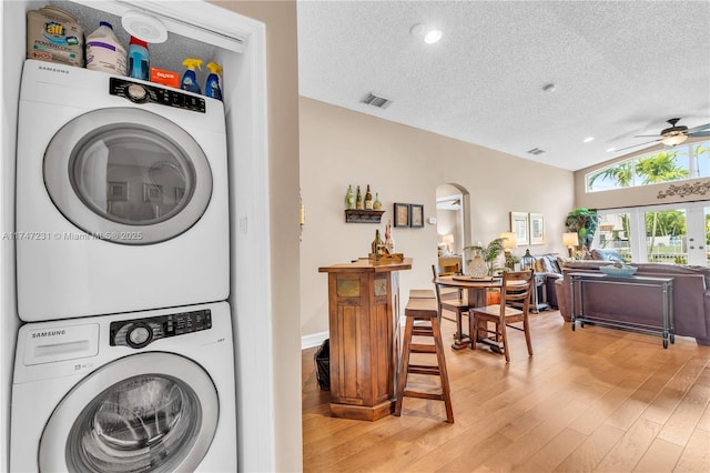 clothes washing area with stacked washer and dryer, laundry area, visible vents, wood finished floors, and a textured ceiling