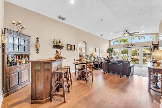 bar with visible vents, light wood-style floors, vaulted ceiling, french doors, and a bar