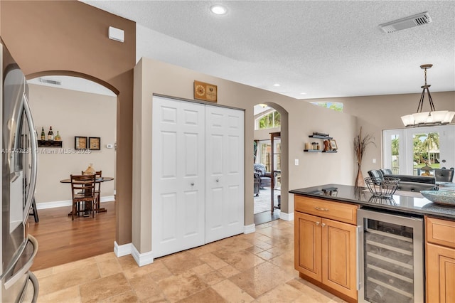 kitchen with beverage cooler, stainless steel refrigerator with ice dispenser, dark countertops, and arched walkways