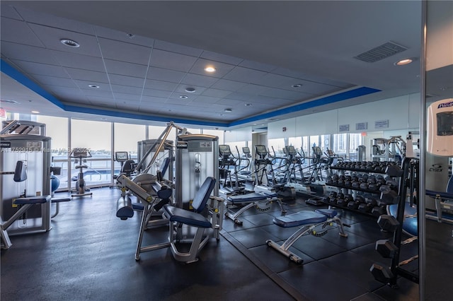 workout area with a paneled ceiling, visible vents, a wall of windows, and a tray ceiling