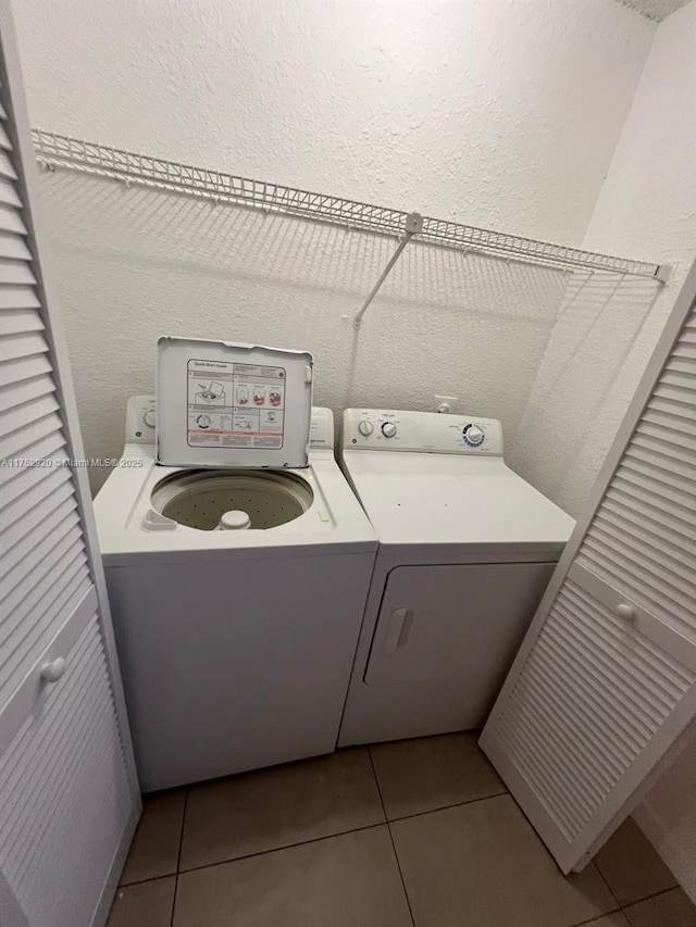 clothes washing area with light tile patterned floors, laundry area, separate washer and dryer, and a textured wall