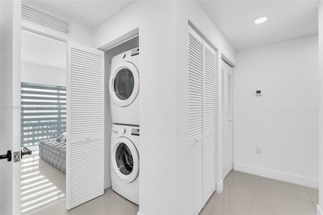 washroom with stacked washer and clothes dryer, light tile patterned floors, baseboards, and laundry area