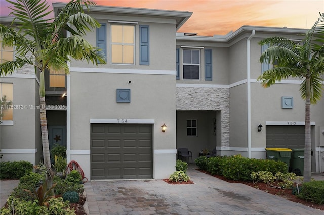 townhome / multi-family property with a garage, stone siding, decorative driveway, and stucco siding