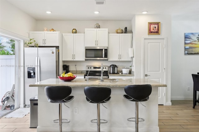 kitchen featuring stainless steel appliances, a sink, a kitchen breakfast bar, white cabinets, and a center island with sink