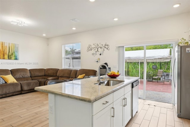 kitchen featuring stainless steel appliances, open floor plan, white cabinets, a kitchen island with sink, and a sink