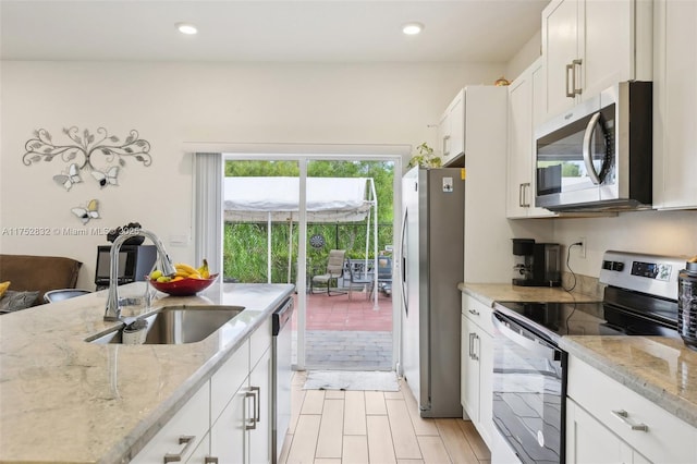 kitchen with light stone counters, white cabinetry, stainless steel appliances, and a sink