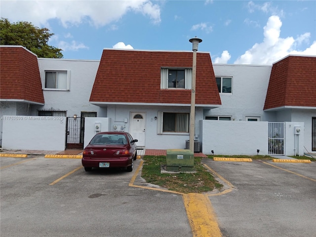 view of property with a gate, roof with shingles, fence, and mansard roof