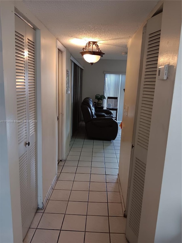 corridor with light tile patterned floors, baseboards, and a textured ceiling