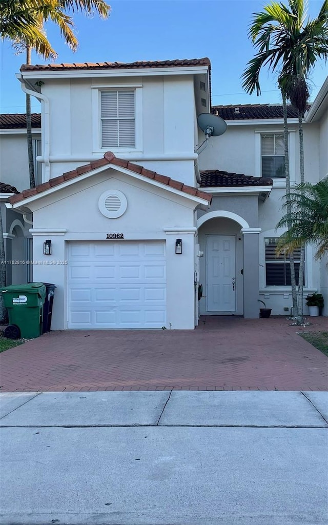 view of front of home with decorative driveway, a tile roof, an attached garage, and stucco siding