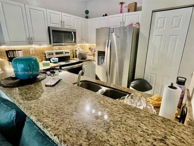 kitchen with stainless steel appliances, a peninsula, a sink, white cabinetry, and backsplash