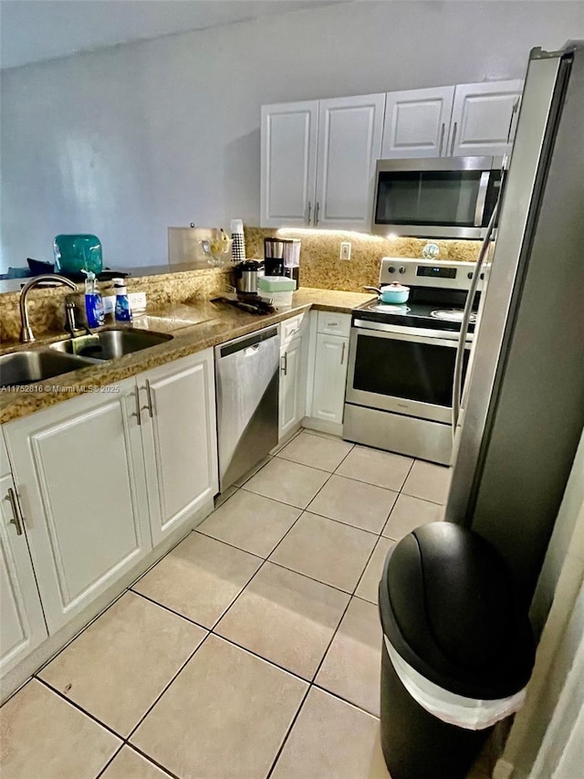 kitchen featuring light tile patterned floors, decorative backsplash, white cabinets, appliances with stainless steel finishes, and a sink