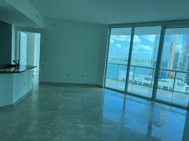 unfurnished room featuring a wall of windows, a view of city, a sink, and baseboards