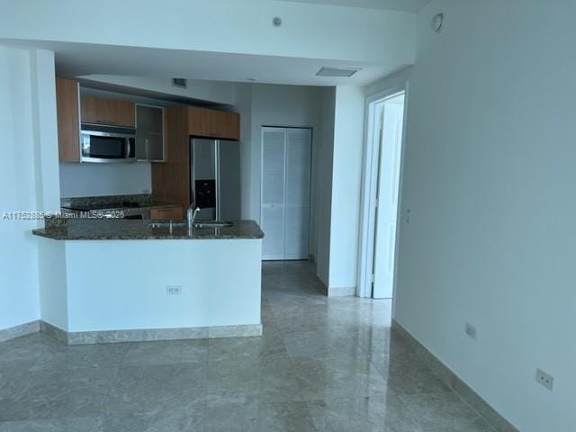 kitchen with brown cabinetry, stainless steel microwave, a peninsula, fridge with ice dispenser, and a sink