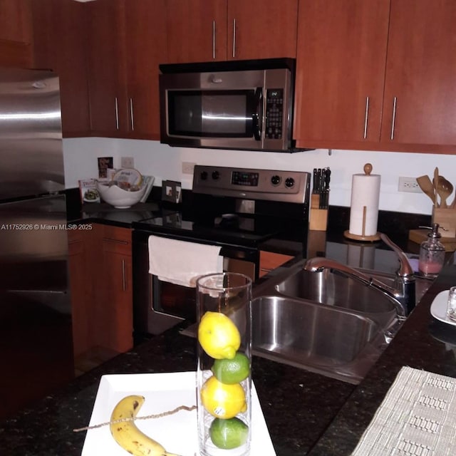 kitchen with appliances with stainless steel finishes, dark countertops, and a sink