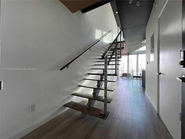 staircase featuring a high ceiling, a wall of windows, wood finished floors, and baseboards