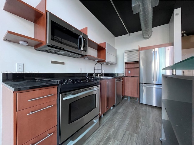 kitchen featuring dark stone counters, dark wood-style floors, appliances with stainless steel finishes, open shelves, and a sink