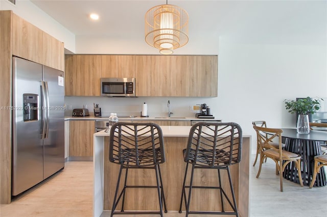 kitchen with decorative light fixtures, light countertops, appliances with stainless steel finishes, a sink, and light wood-type flooring