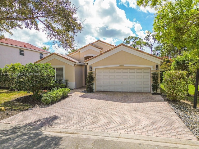 mediterranean / spanish home featuring an attached garage, a tiled roof, decorative driveway, and stucco siding