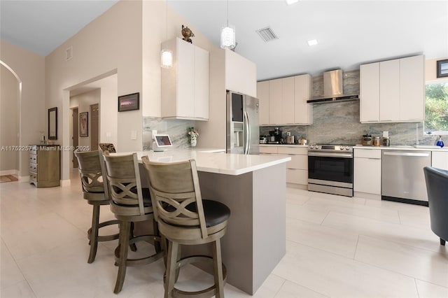 kitchen featuring wall chimney exhaust hood, a kitchen breakfast bar, decorative light fixtures, light countertops, and stainless steel appliances