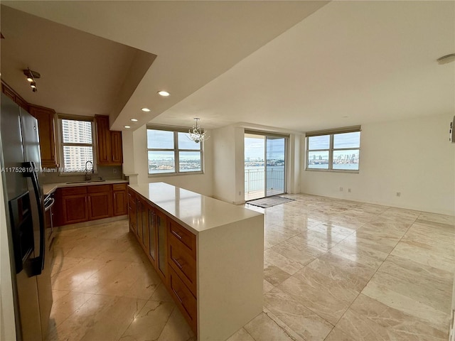 kitchen featuring a center island, decorative light fixtures, stainless steel refrigerator with ice dispenser, light countertops, and a sink