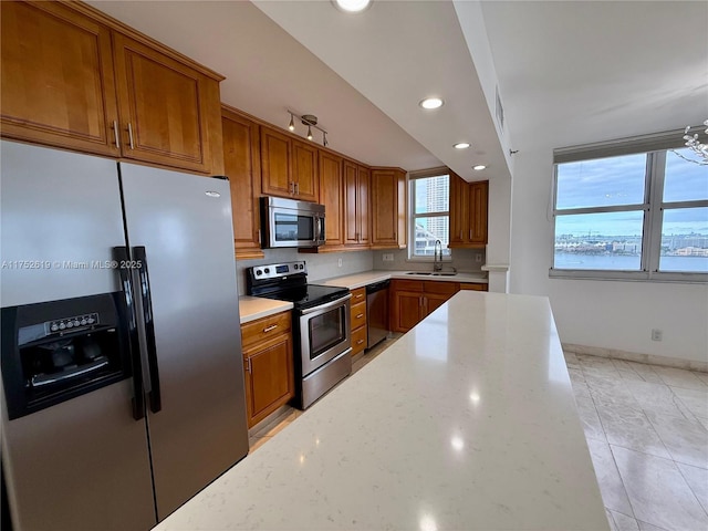 kitchen with stainless steel appliances, brown cabinetry, a sink, and light stone counters