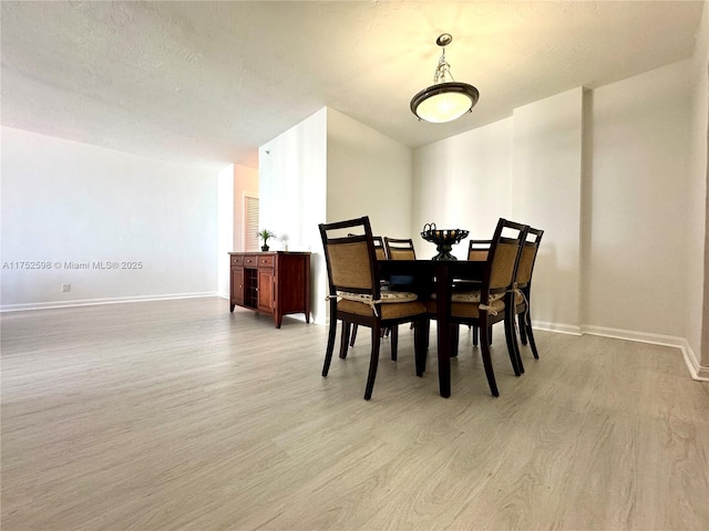 dining space featuring baseboards, a textured ceiling, and light wood-style floors