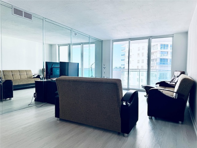 living room featuring floor to ceiling windows, visible vents, a textured ceiling, and wood finished floors