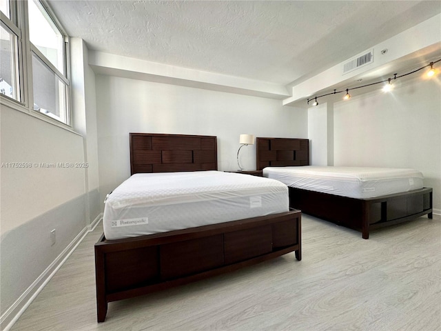 bedroom featuring baseboards, visible vents, light wood-style flooring, rail lighting, and a textured ceiling